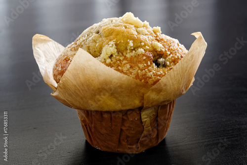 Whole baked blueburry muffin in baking paper cup isolated on black wooden table.