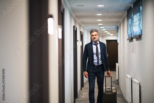 Mature businessman walking with luggage in a hotel corridor.