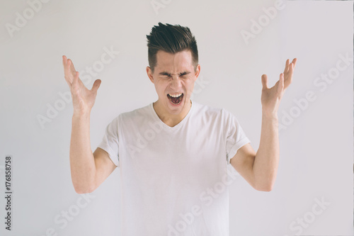 Young black-haired nerd guy wearing white t-shirt holding hands on head and going to cry while found out about something horrorful. Crying man with glasses having troubles photo