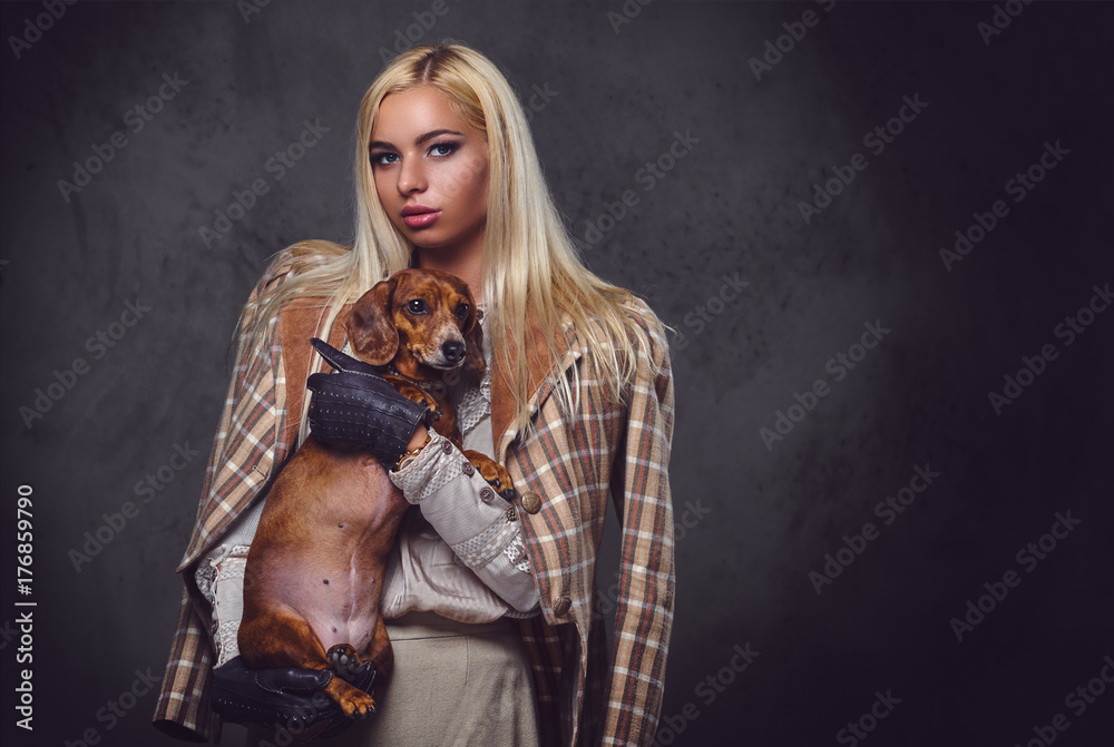 A stylish blonde female holds a red badger dog.