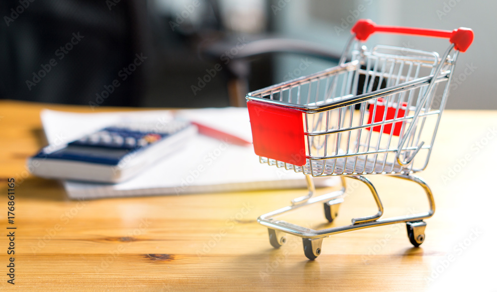 Budget of poor and low income family. Rising food and grocery store prices and expensive daily consumer goods concept. Miniature shopping cart and trolley on table with calculator, pen and paper. 