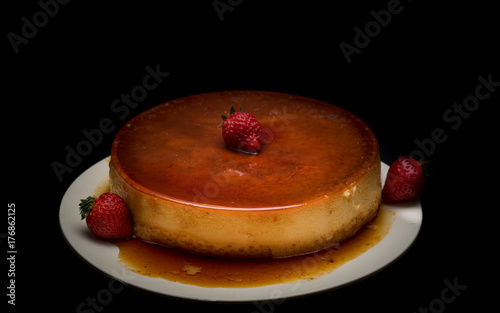 Flan recien hecho adornado con fresas y caramelo en fondo negro