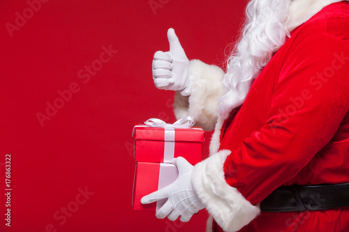 christmas Photo of Santa Claus gloved hand with red giftbox. thumb up