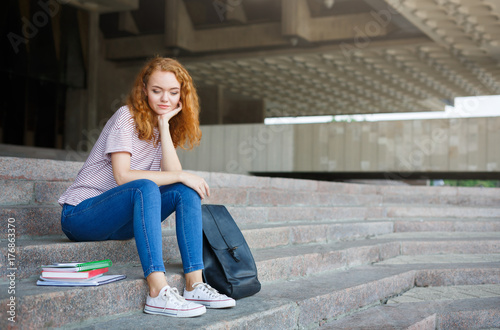 Young redhead student girl sitting on the stairs outdoors
