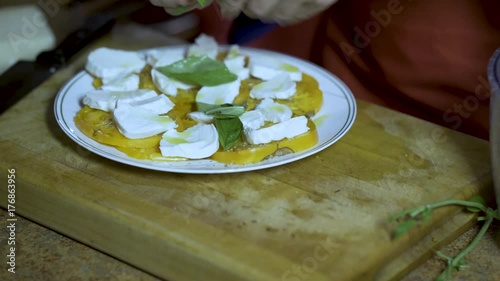 On a thick wood cutting board a chef take fresh basic out of a salad spinner and tears it and arranges it on the caprese salad of yellow heirloom tomatoes and fresh mozzarella. photo