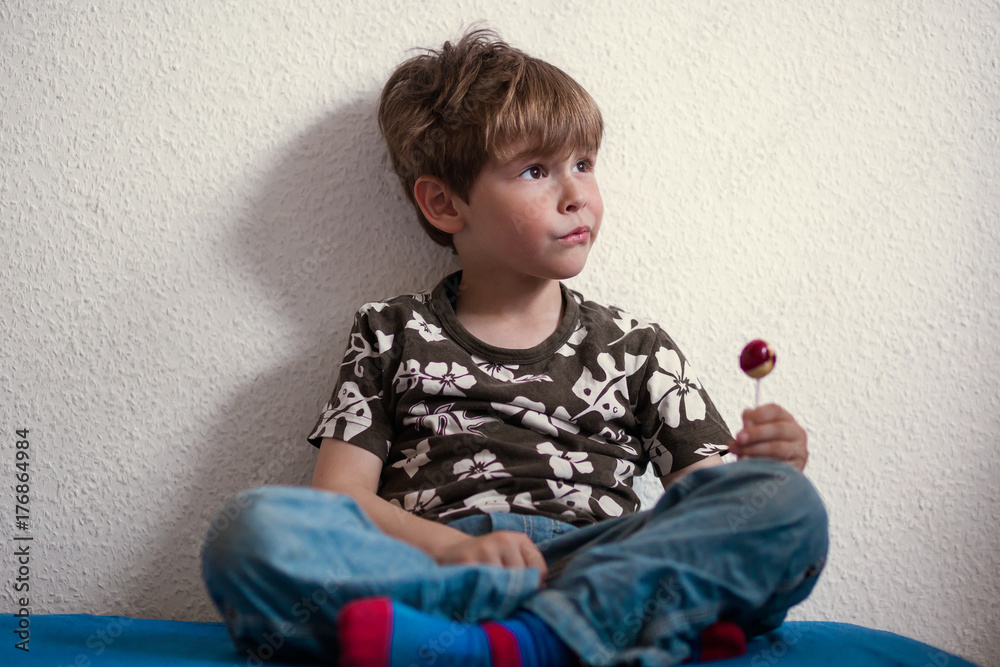 Preschool boy sitting cross legged on bed with lollipop Preschool boy sitting cross legged on bed with lollipop