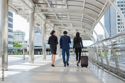 businessman and businesswoman walk together with mobile tablet and luggage on the public street, business travel