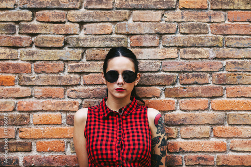 Young alternative woman standing in front a brick wall.