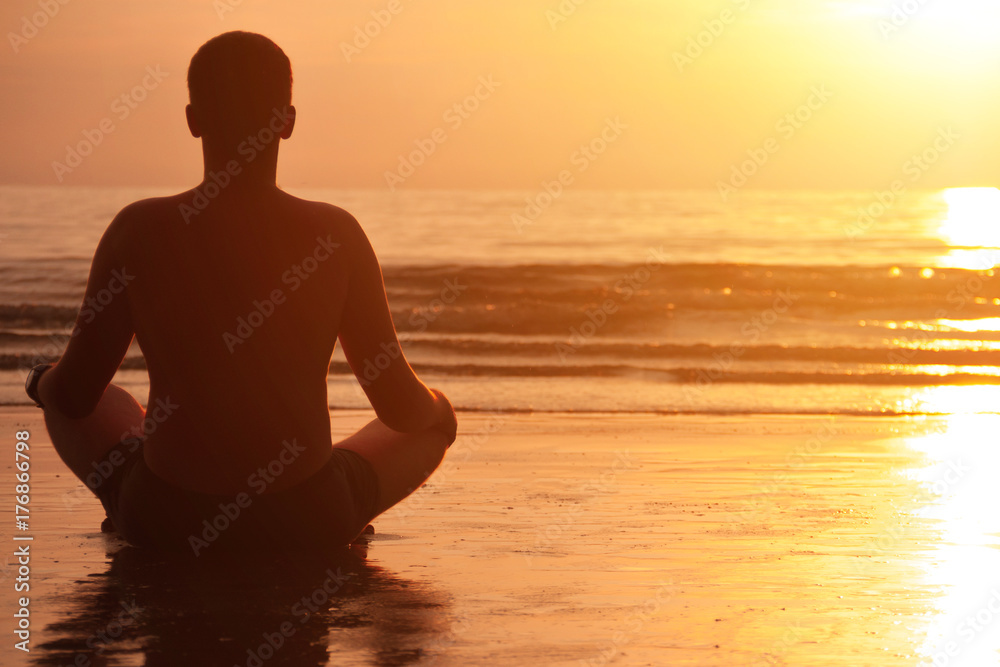 Silhouette of young man meditating at sunset beach