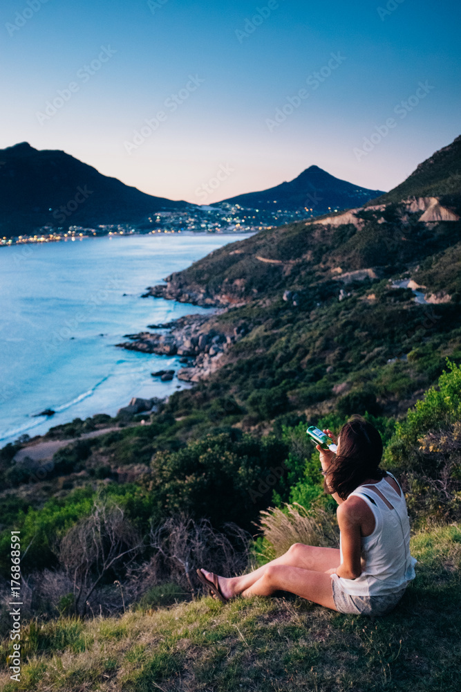 Woman sitting having a drink whilst enjoying dusk overlooking a beautiful coastal valley Woman sitting having a drink whilst enjoying dusk overlooking a beautiful coastal valley