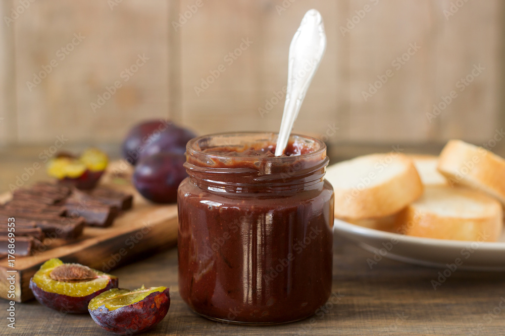 Plum chocolate jam in a glass jar, fresh plums and pieces of chocolate on a wooden surface. Plum chocolate jam in a glass jar, fresh plums and pieces of chocolate on a wooden surface.