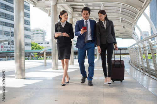 businessman and businesswoman talk and walk together with mobile tablet and luggage on the public street, business travel