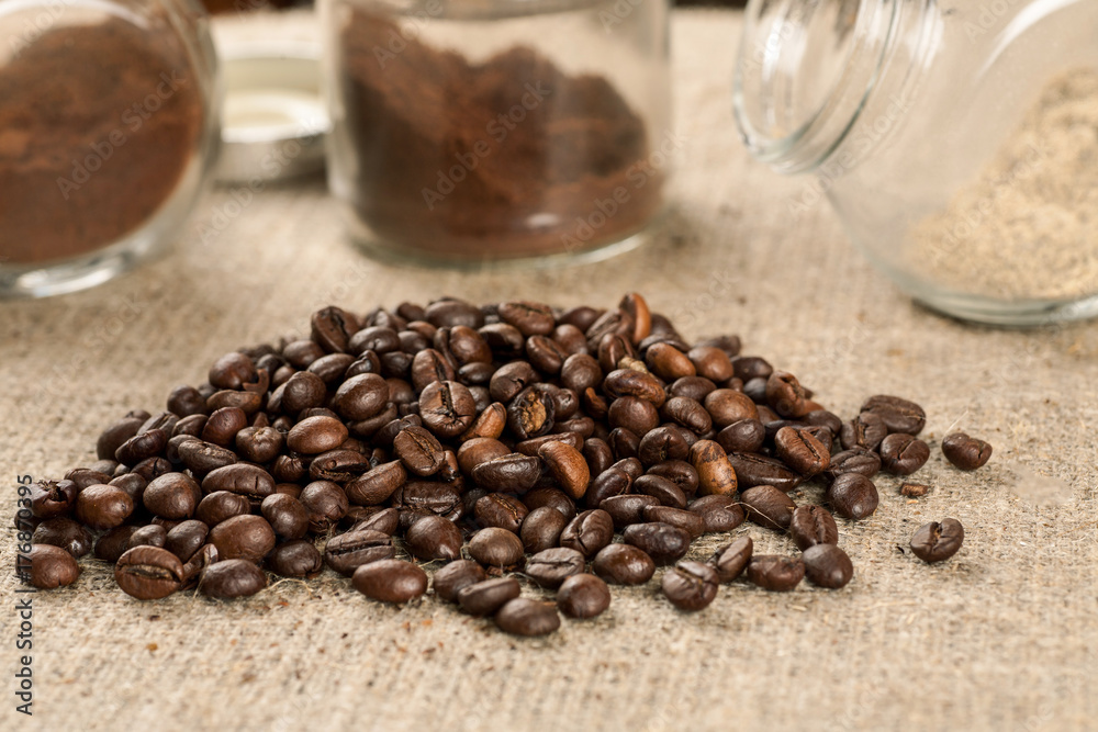 Pile of roasted coffee beans and glass jars with ground coffee Pile of roasted coffee beans and glass jars with ground coffee