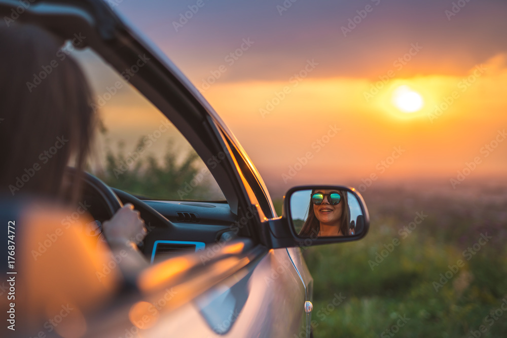 The happy woman sit in a car on the background of the sunset
