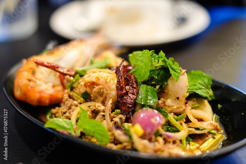 Big shrimps and squids and spicy minced pork mixed together with various herbs and vegetables including dried chilli served on black plate, for thai food background or texture.