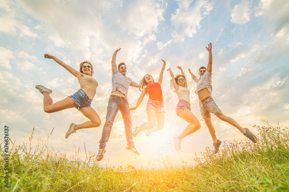 The happy friends jumping on the grass on the sunny background The happy friends jumping on the grass on the sunny background