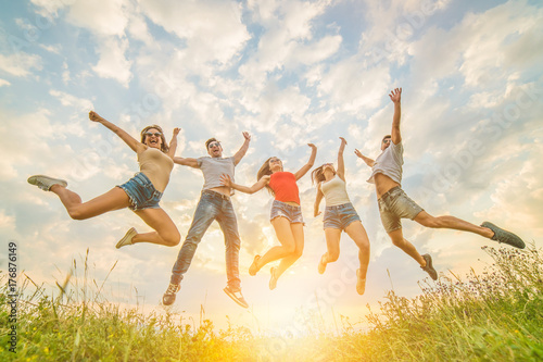 The five friends jumping on the grass on the sunny background
