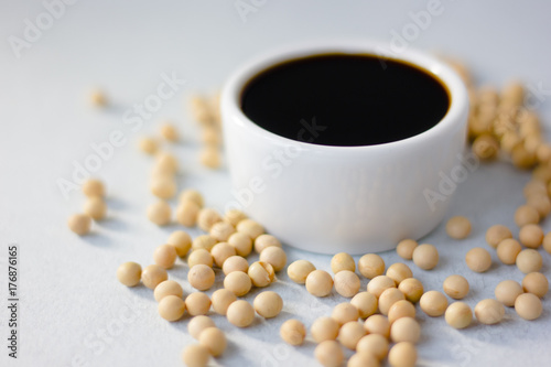 Soybean sauce surrounded by soy beans over white background.