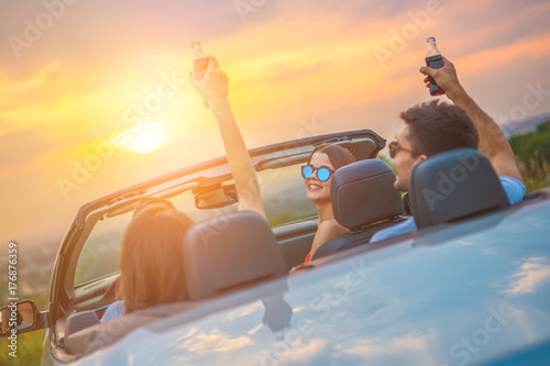 The happy people sit in a cabrio on the bright sun background