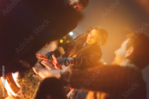 The happy friends warming hands near a bonfire. evening night time