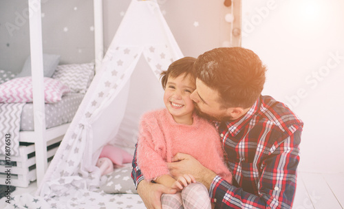 Cute little daughter and her handsome young dad iare playing together in child's room. Dady and child spend time together while sitting on the floor in bedroom