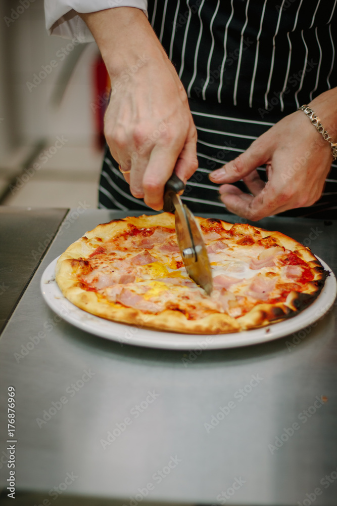 Chef cutting pizza with the round pizza cutter or knife.