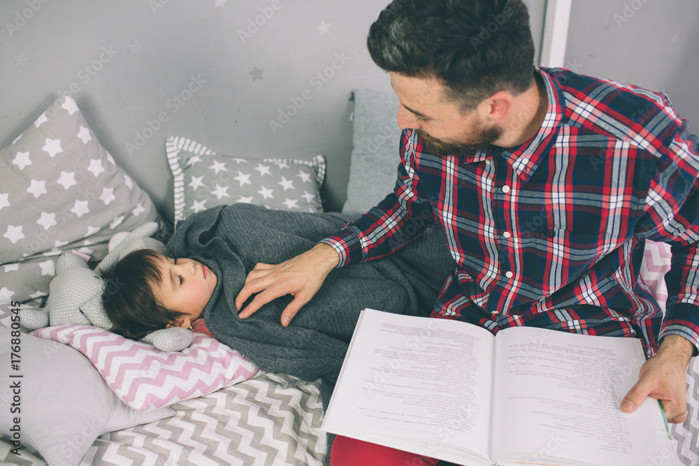 Father reading a book to his daughter while lying on the bed in bedroom Father reading a book to his daughter while lying on the bed in bedroom