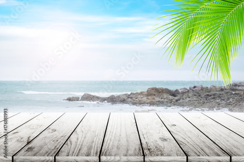 Empty wooden table and coconut leaves with party on beach blurred background in summer time. © Akura Yochi