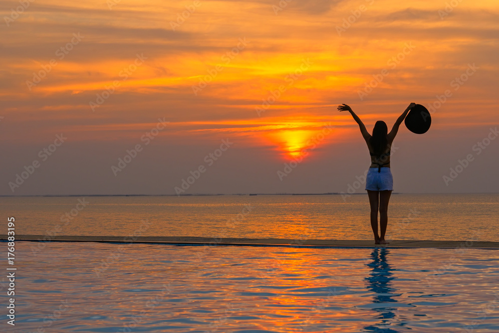 Smilling asina woman happy in big hat relaxing on the swimming pool, travel near the sea and beach in the sunset. Summer Concept