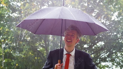 Businessman sheltering underneath an umbrella in the rain