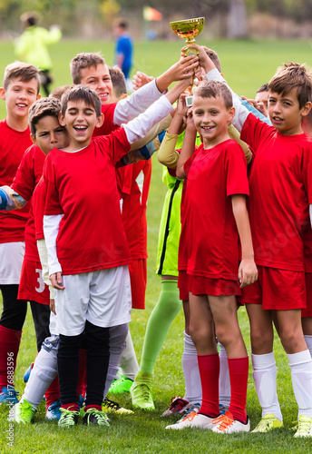 Kids soccer football - children players celebrating with a trophy after match on soccer field