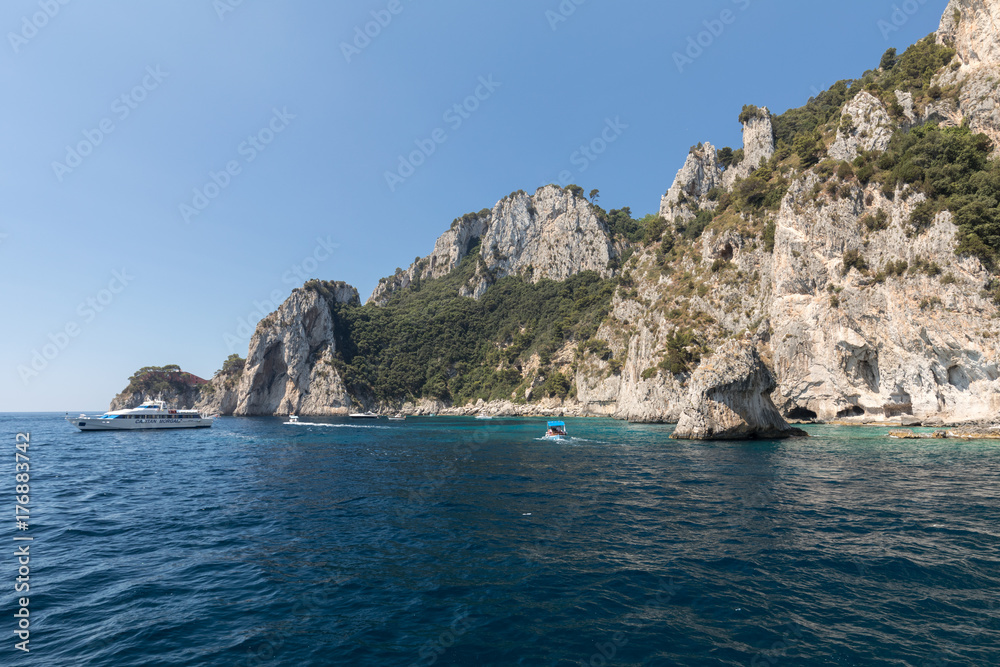  View from the boat on the Boats with tourists and the cliff coast of Capri Island. Italy