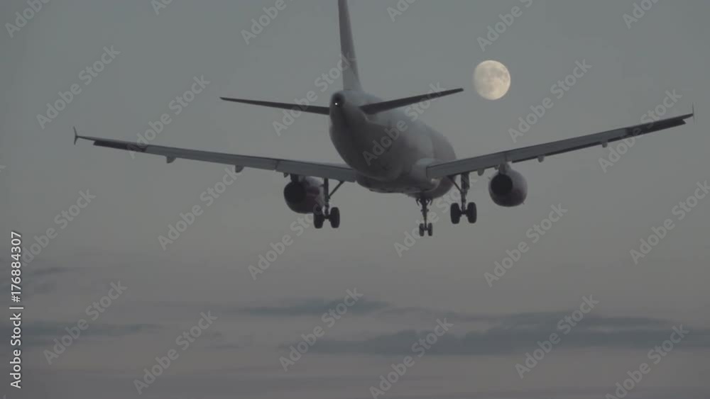 Jet landing at dusk against full moon in slow motion Jet landing at dusk against full moon in slow motion