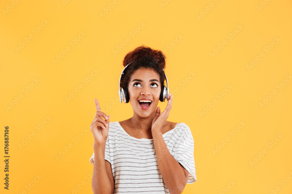 Happy african lady in headphones looking and pointing up at copy space isolated Happy african lady in headphones looking and pointing up at copy space isolated
