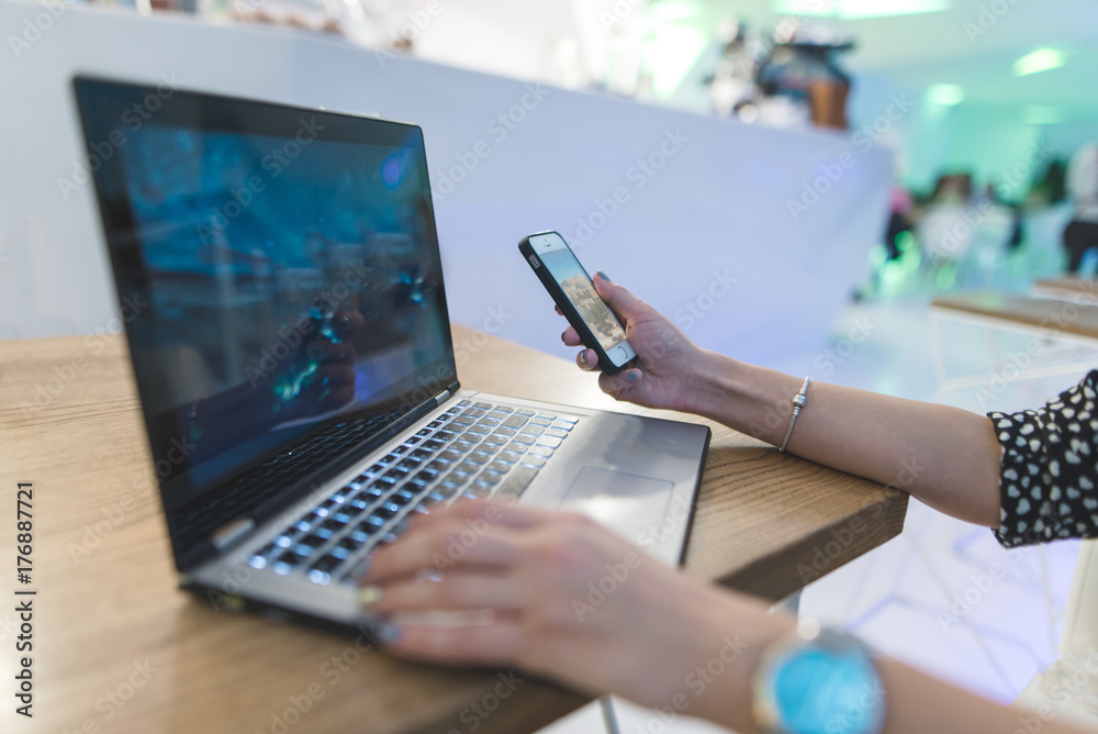 Woman's hand with phone in hand against laptop and coffee background. Business concept. Business woman in a cafe. Woman's hand with phone in hand against laptop and coffee background. Business concept. Business woman in a cafe.