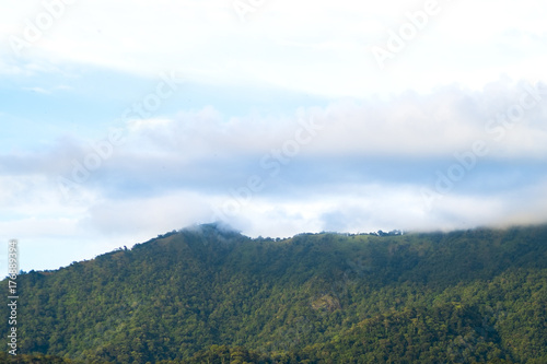View from below, Looking to beautiful green mountain covered with white mist on the top and yellow light with blue sky and some clouds, After the rain at sunset. North of Thailand.
