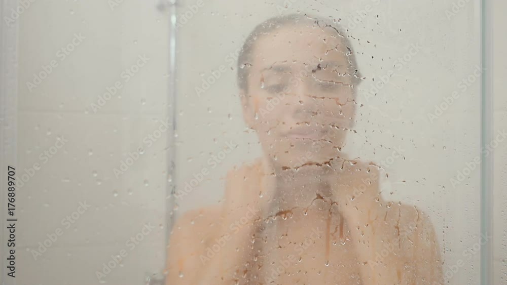 Pretty lady enjoys hot water in the shower cabin