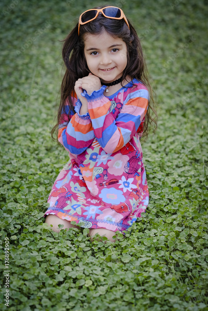 Small girl with glasses sitting inside green grass Small girl with glasses sitting inside green grass