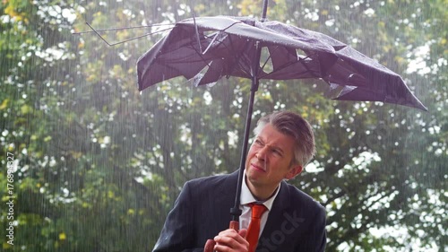 Businessman sheltering underneath a broken umbrella in the rain
