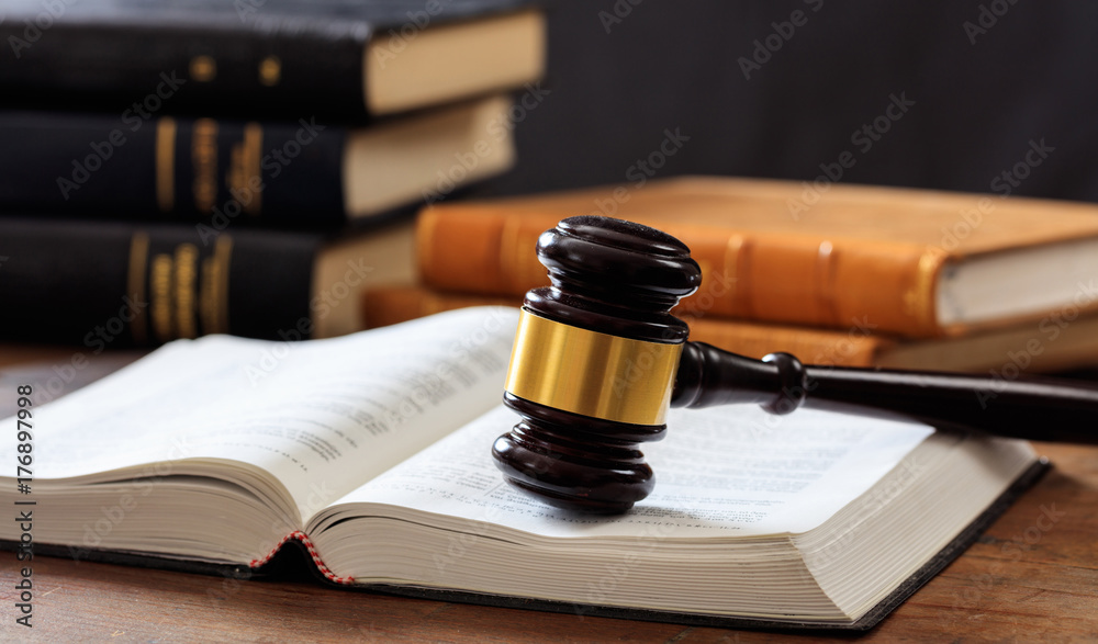 Judge gavel on an open book, wooden desk, law books background Judge gavel on an open book, wooden desk, law books background