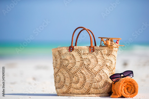 Beach accessories - toy plane, straw bag, orange towel and unglasses on the beach
