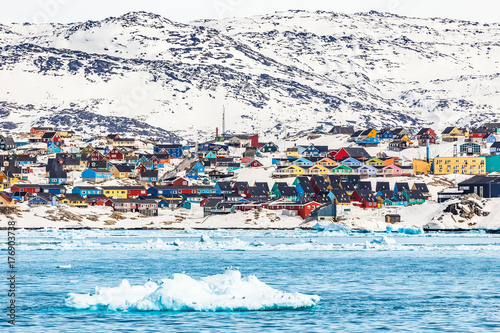Arctic snow city panorama with colorful Inuit houses on the rocky hills covered in snow with icebergs in the foreground, Ilulissat, Greenland photo