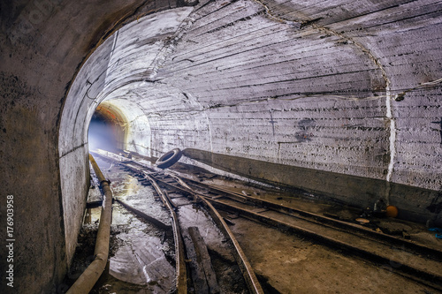 Bifurcation of rusty narrow-gauge railway. Tunnel in abandoned mine. Turn the tunnel. Light from the turn. 