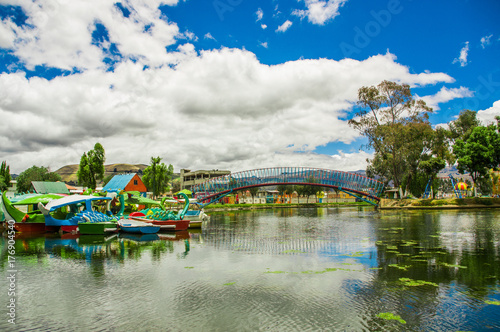 Beautiful day of an artificial lake located in the midle of a park, with some boats of animals in the water with the reflection in the city of Cayambe, Ecuador photo