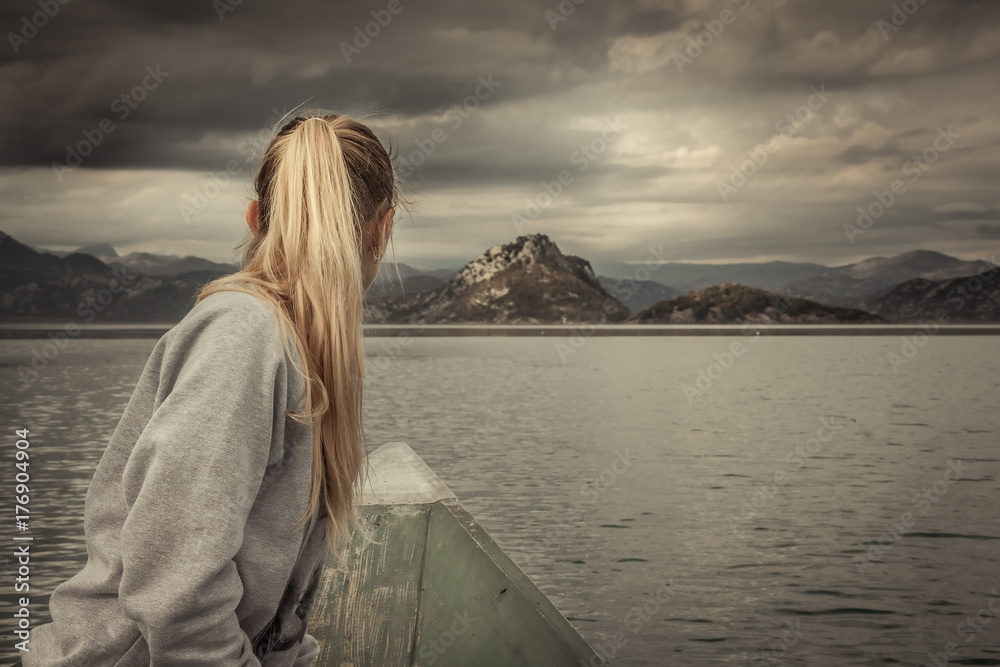 Woman traveler sailing on boat towards shore with with Mountains landscape on horizon in overcast day with dramatic sky  