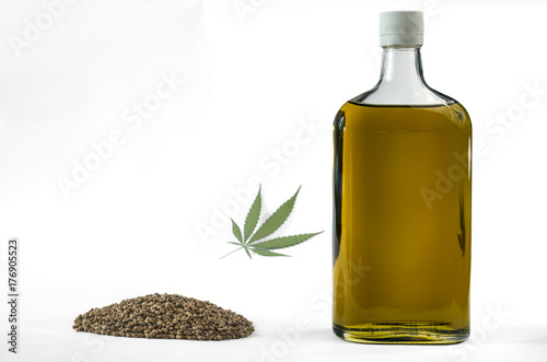 Hemp seeds in a bottle with a bunch of marijuana seeds and a marijuana leaf. Isolated on white background.