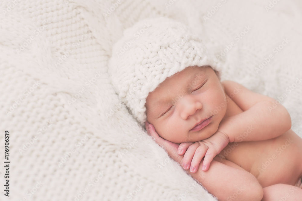 Beautiful newborn baby sleeping peacefully on a white blanket wearing a matching hat Beautiful newborn baby sleeping peacefully on a white blanket wearing a matching hat