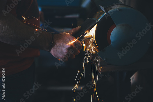 Close up of man sharpening an axe with a grinder - vertical photo