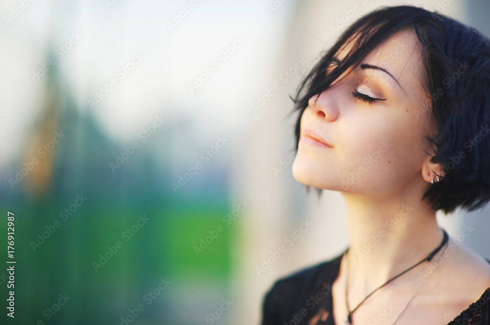 Young beautiful brunette woman, eyes closed, enjoying the bright warm day, on blurred background, close up