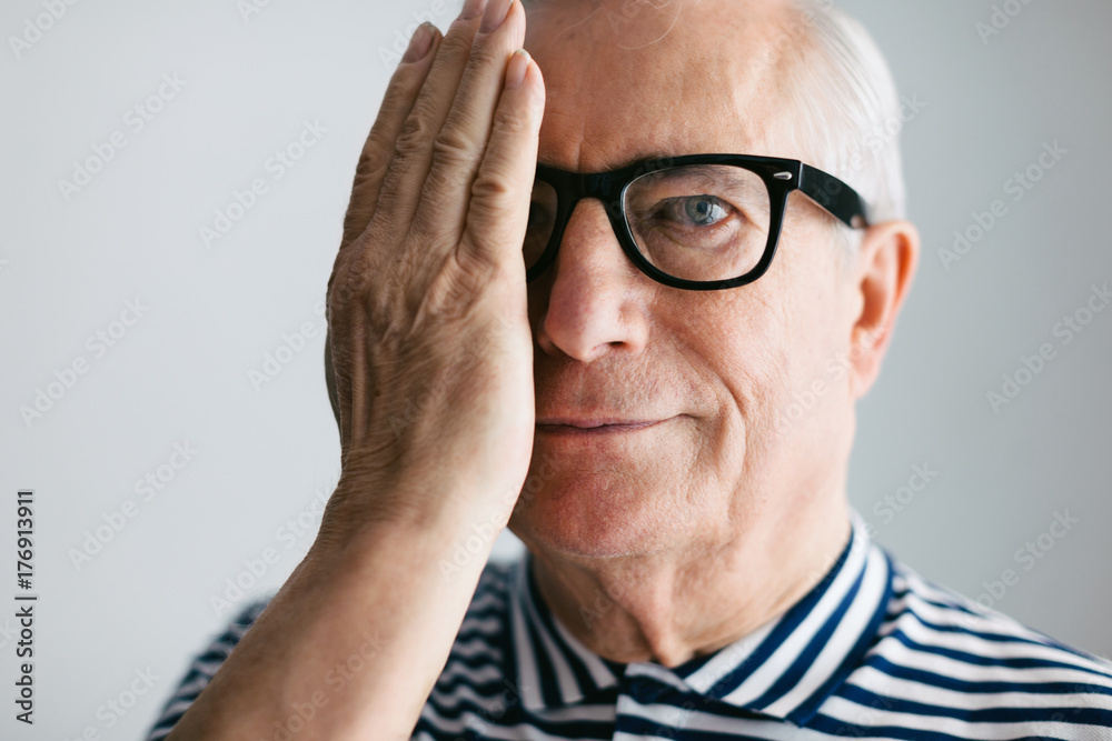 Portrait of an elderly man covering his eye with a hand and smiling. Portrait of an elderly man covering his eye with a hand and smiling.